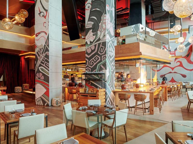 Světle moderní restaurace s dřevěným a bílým nábytkem a výraznými nástěnnými malbami.