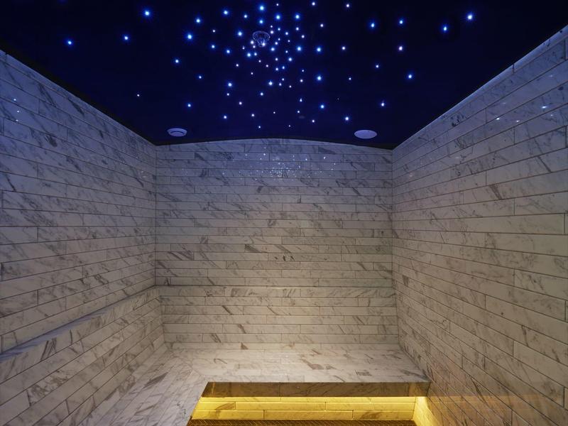 Moderní wellness prostor s osvětlením, mramorovými stěnami a zlatým vložením na podlaze.