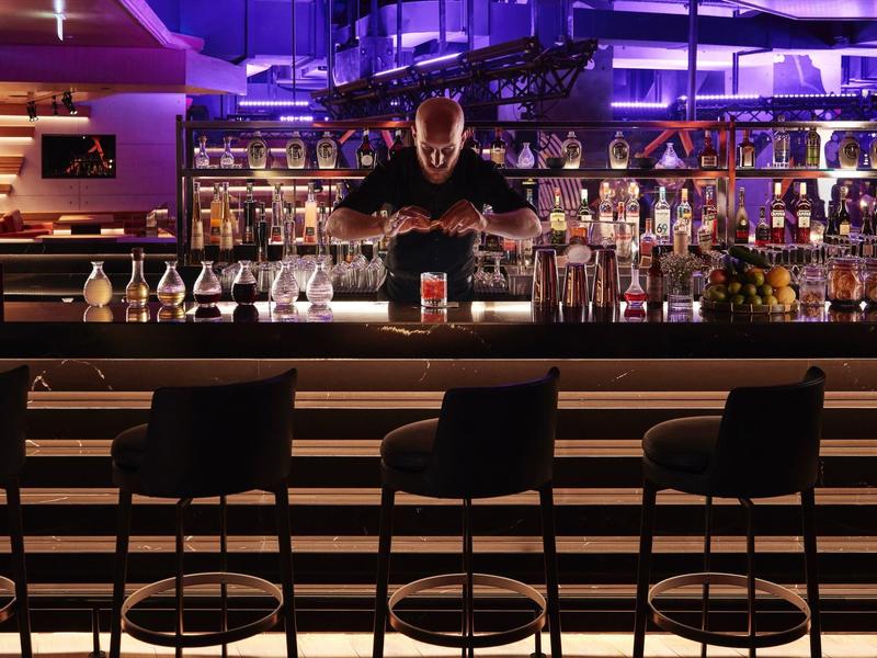 Barman připravující drinky ve stylovém baru s fialovým osvětlením.