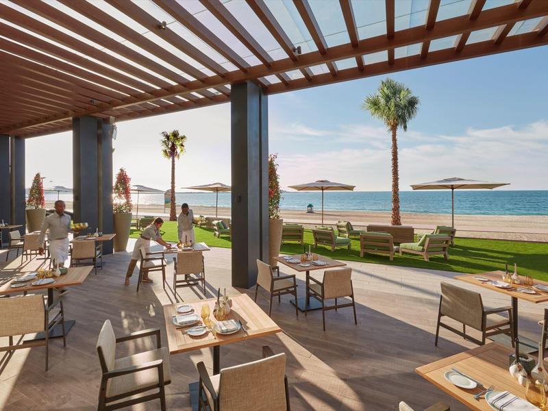 Otevřená terasa restaurace s výhledem na pláž a moře za slunečného počasí.