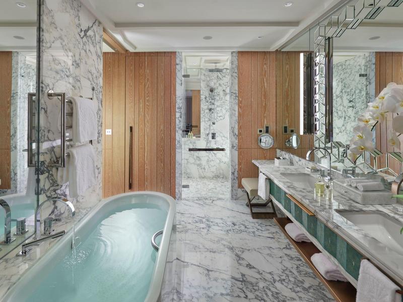 Luxusní koupelna s volně stojící vanou, mramorovými stěnami a dvojitými umyvadly.