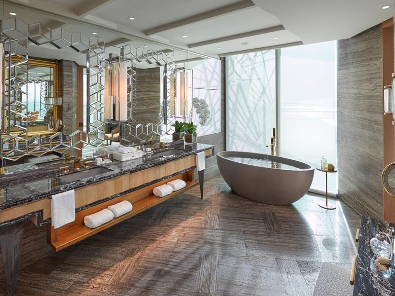 Elegantní koupelna s volně stojící vanou, velkým zrcadlem a tmavou mramorovou podlahou.