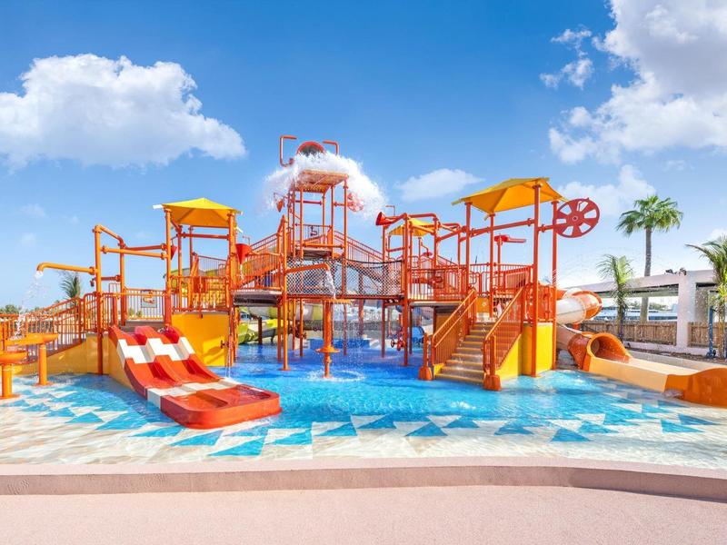 Colorful water playground with slides and sprinklers under a blue sky at the hotel.