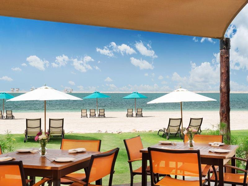 Terrace with tables and umbrellas on the beach with sea view under blue sky.