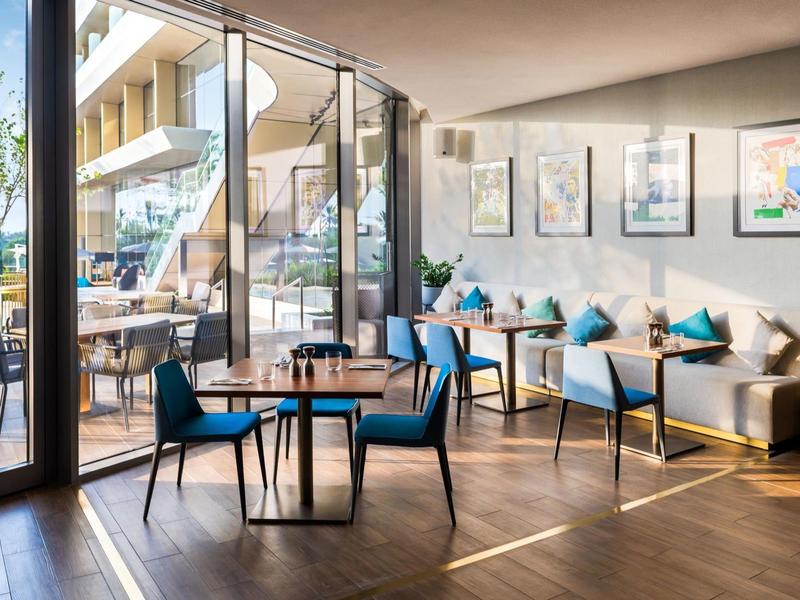 Modern café with blue chairs, tables, and large windows opening to a terrace.