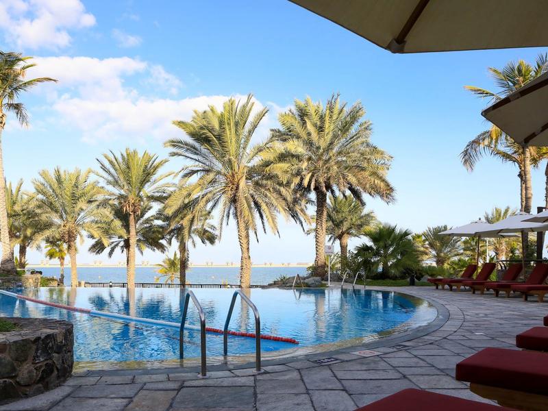 Pool with palm trees and lounge chairs under umbrellas on a clear sky