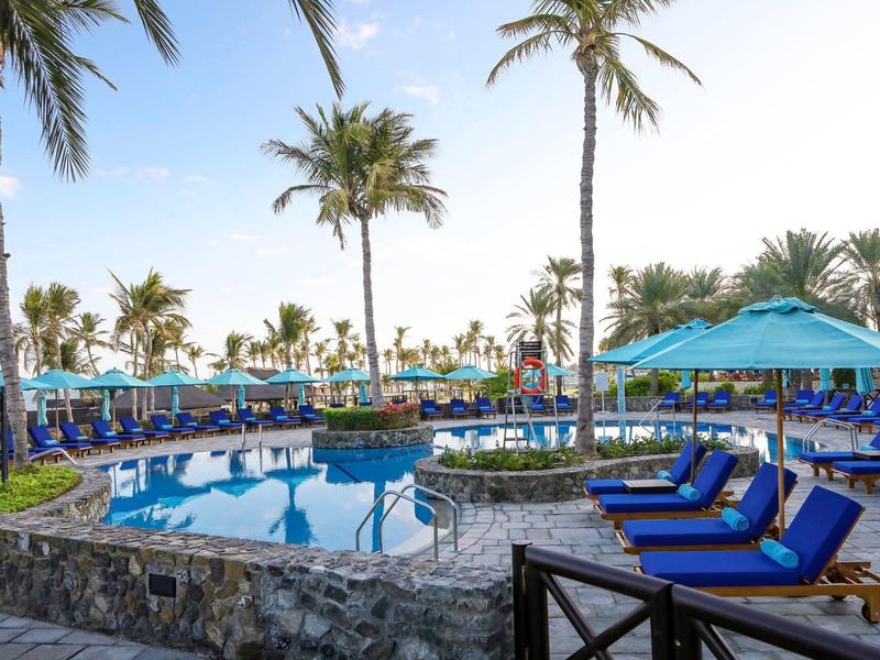 Pool area with lounge chairs and palm trees in a tropical hotel resort.
