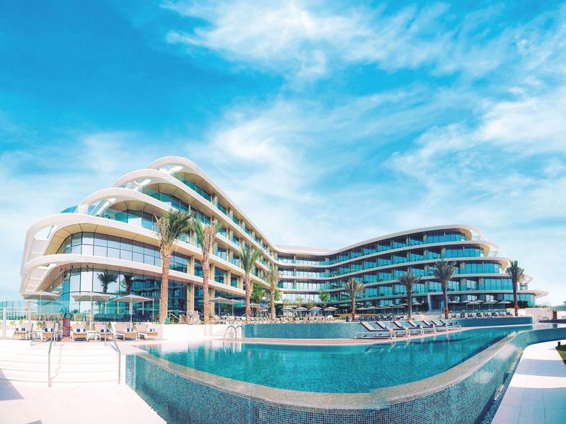 Modern hotel with curved architecture and large pool under a blue sky.
