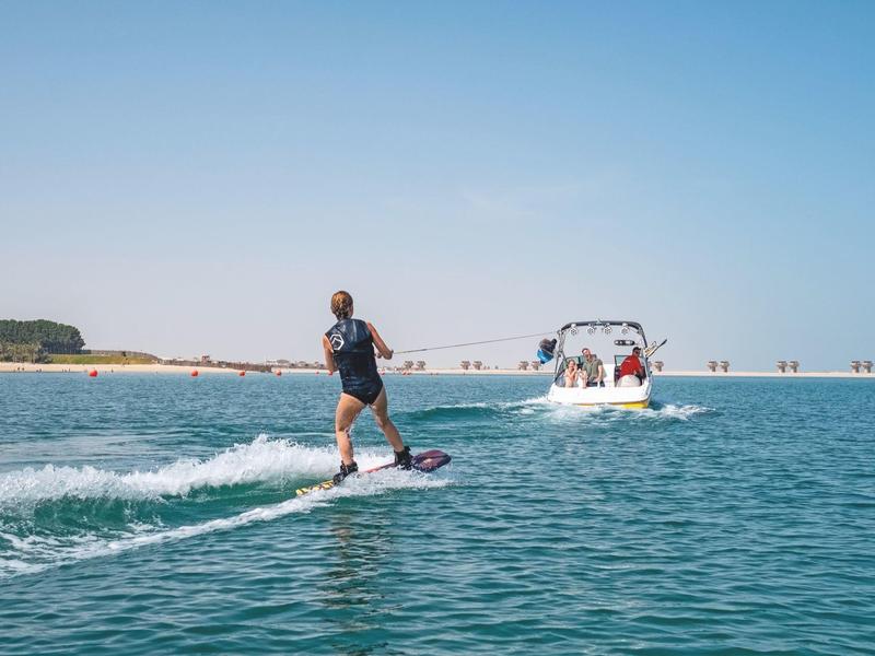 Person surfing on an electric surfboard behind a motorboat on open water.