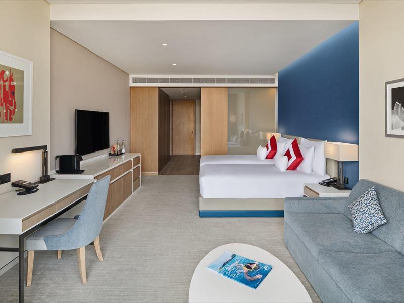 Modern hotel building with palm trees and a walkway in the foreground on a sunny day.