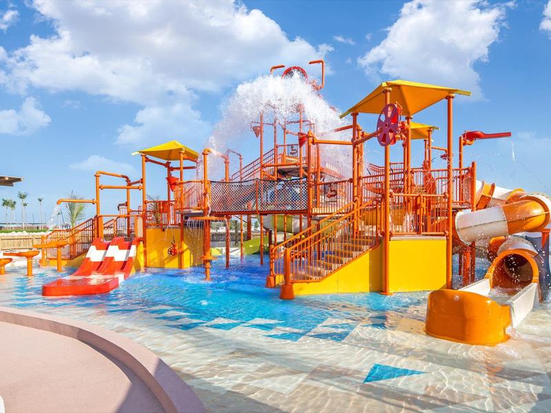 Colorful water playground with slides and spray features under a blue sky.