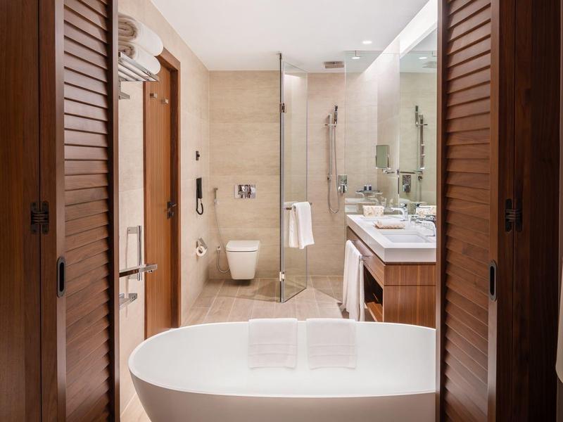 Bathroom with freestanding bathtub and wooden doors in a modern hotel room.