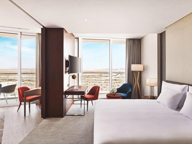 Modern hotel room with large bed, seating area, and floor-to-ceiling windows with view.