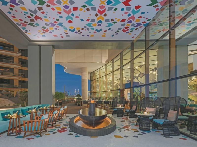 Moderner Außenbereich mit buntem geometrischem Muster an Decke und Boden, Sitzgruppen und Glaswänden.