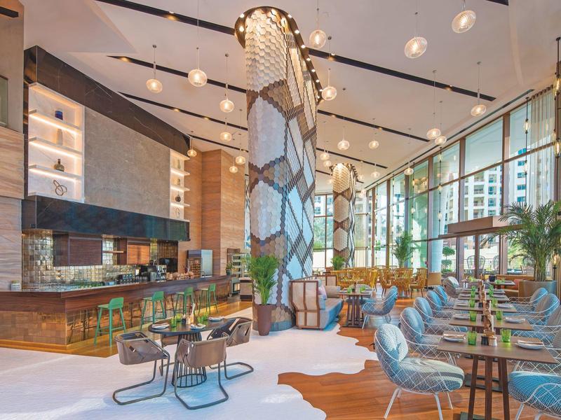 Modernes Hotelrestaurant mit hohen Decken, großen Fenstern, hölzernen Akzenten und bunten Sitzmöbeln.