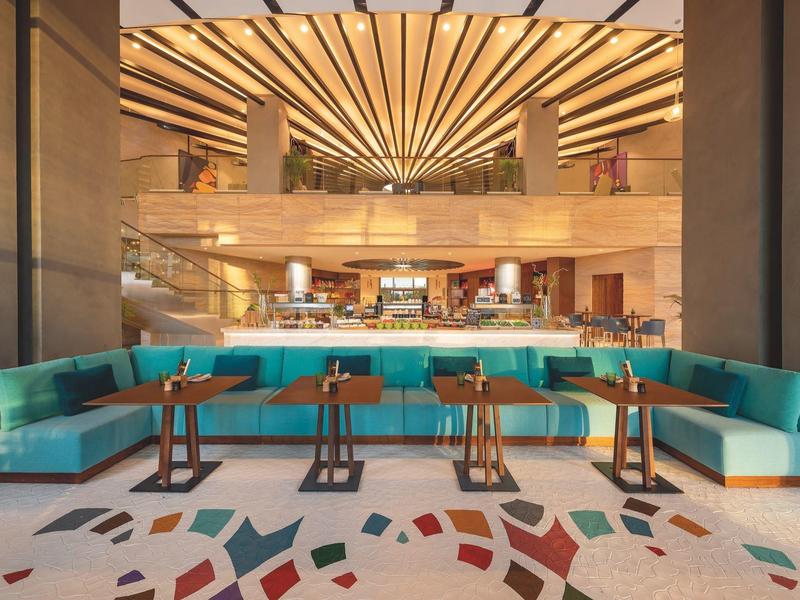 Moderner Gastraum mit türkisen Sofas, Holz-Tischen, buntem Fliesenboden und strahlenförmiger Decke.