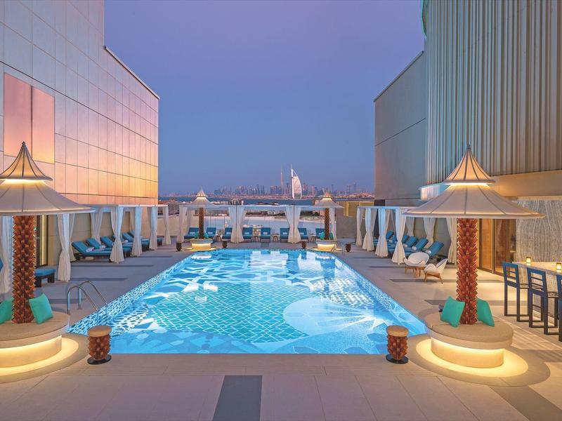 Moderner Außenpool mit Liegestühlen und Bar, beleuchtet in sanften Blautönen in der Abenddämmerung.