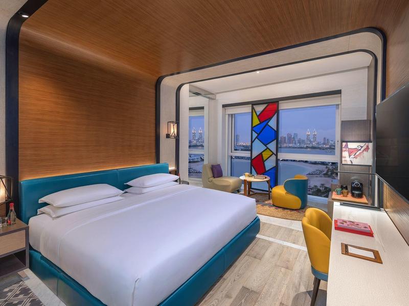 Modernes Hotelzimmer mit großem Bett, buntem Raumteiler und Panoramafenster mit Stadtblick.