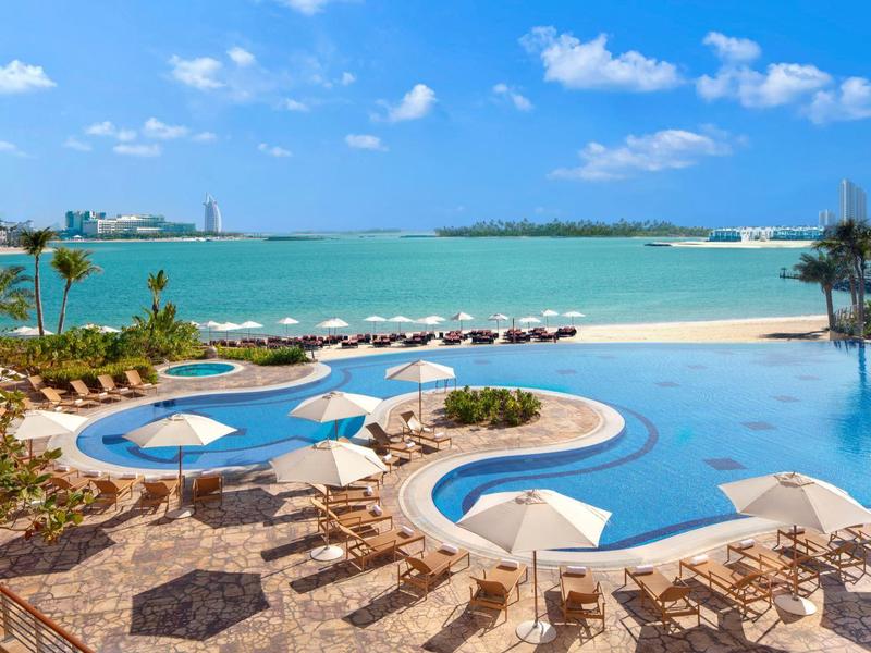 Großer Außenpool mit Sonnenschirmen, Liegestühlen und Blick auf Meer und blauen Himmel.