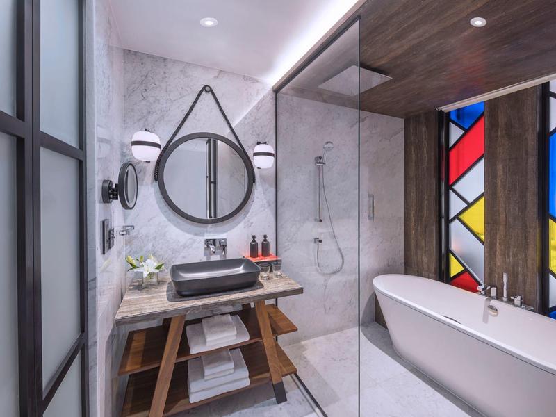 Modernes Bad mit freistehender Badewanne, rundem Spiegel, Mosaikfenster und Marmorwänden.