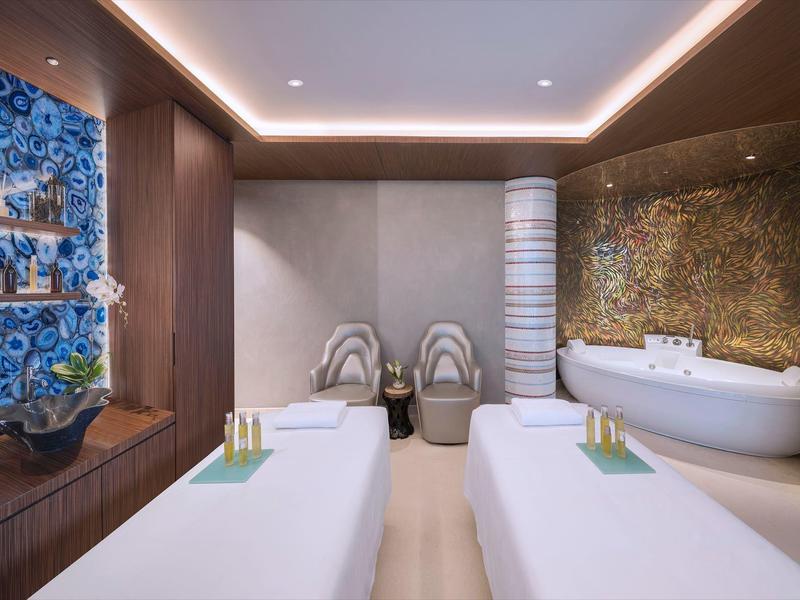 Moderner Spa-Raum mit zwei weißen Massageliegen, warmem Holzdekor und beruhigender Beleuchtung.