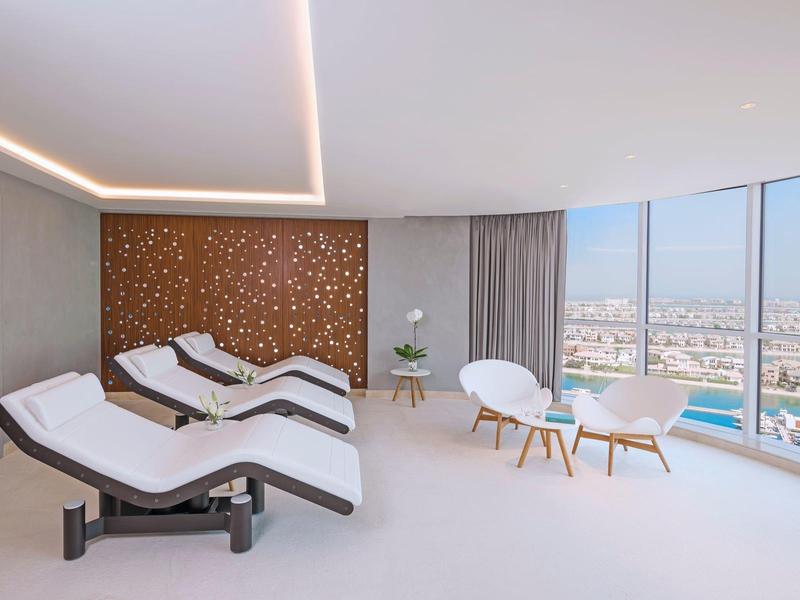 Helles Zimmer mit großen Panoramafenstern, sechs Liegestühlen und drei Sesseln mit Tisch.