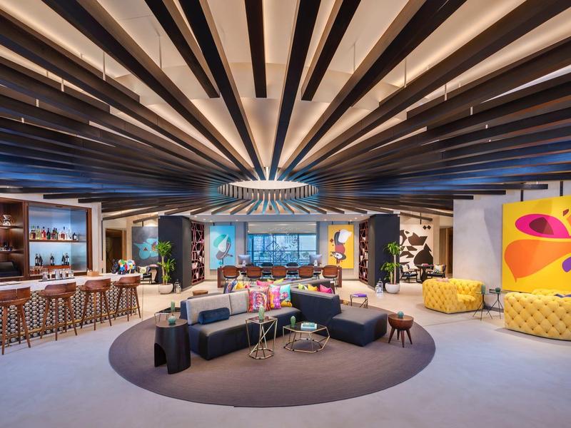 Modernes Loungezimmer mit schwarzer Ledercouch, gelben Sesseln und Bar unter Holzdeckenbalken.