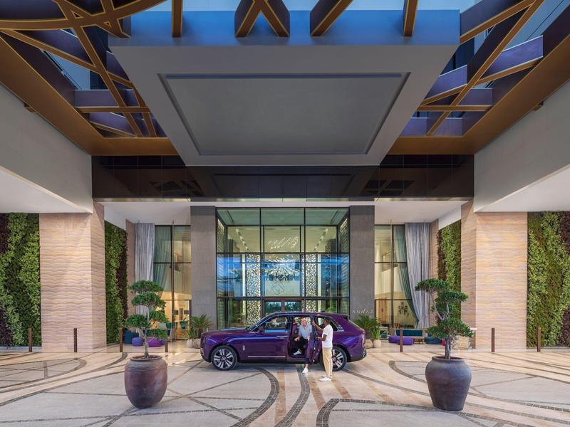 Luxushotel-Eingang mit Glasdach, grünen Wandpflanzen und lila Auto daneben auf Marmorboden.