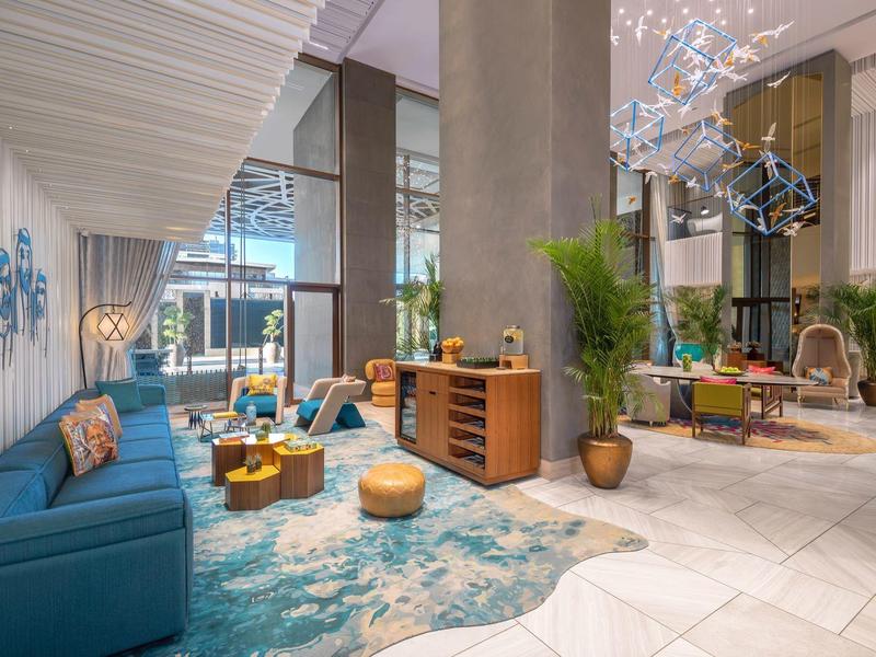 Moderne Lobby mit blauen Sofas, Teppich, Holzkommode, Pflanzen und großem Fenster für Tageslicht.