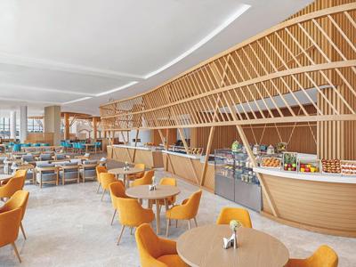 Moderner, hell erleuchteter Gastraum mit orangefarbenen Sesseln und Holz-Bar mit Gitterstruktur.