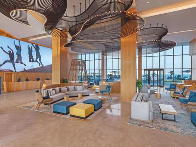 Großer, heller Lounge-Bereich mit modernen Sofas, bunten Hockern und bodentiefen Fenstern.