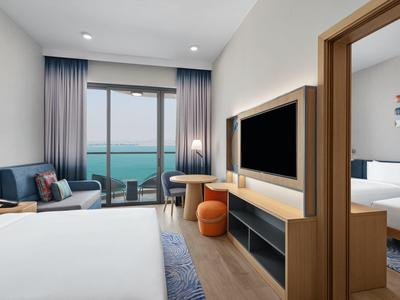 Modernes Hotelzimmer mit Meerblick, Doppelbett, Sitzbereich, Fernseher und angrenzendem Schlafzimmer.