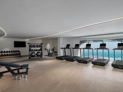 Moderner Fitnessraum mit Laufbändern, Hanteln und großen Fenstern mit Meerblick.