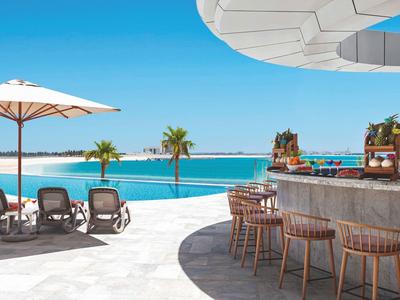 Moderner Poolbereich mit Holzstühlen, Liegestühlen, Sonnenschirm und Blick auf das blaue Meer.