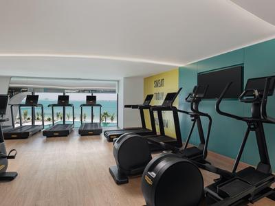 Moderner Fitnessraum mit Laufbändern, Crosstrainern und Meerblick durch große Fenster.