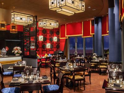 Luxuriöses Restaurant mit roten Wänden, blauen Vorhängen und edlen Holzstühlen bei Dämmerung.