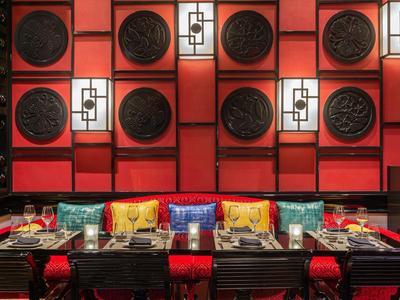 Rot-schwarzes asiatisches Restaurant mit dekorativen runden Wandreliefs und bunten Sitzkissen.