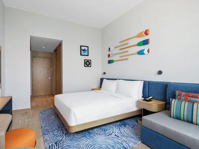 Modernes Schlafzimmer mit Doppelbett, blauem Teppich, Wanddeko aus bunten Paddeln und Sitzbank.