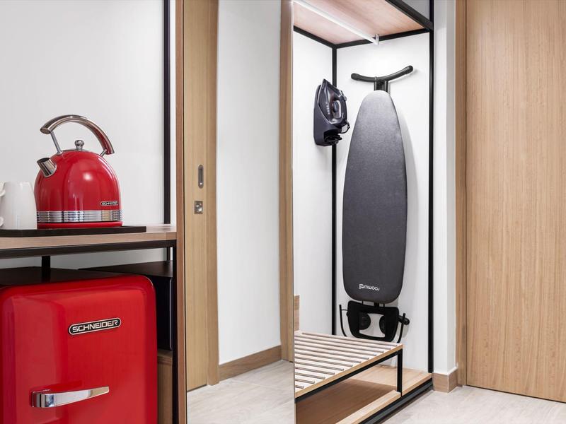 Moderner Flur mit Spiegel, Bügelbrett, Garderobe und rotem Kühlschrank mit Wasserkocher.