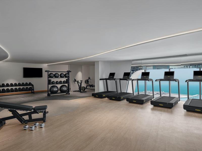 Moderner Fitnessraum mit Laufbändern, Hanteln und großen Fenstern mit Meerblick
