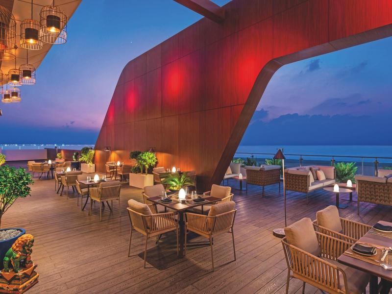 Abendliche Terrasse mit gedeckten Tischen und modernem rote Architektur am Meer.