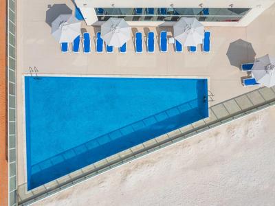 Dreieckiger Außenpool mit blauen Liegestühlen und Sonnenschirmen auf hellem Boden.