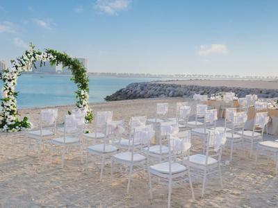 Freie weiße Stühle und ein Blumenbogen am Strand mit Blick auf das ruhige blaue Meer.