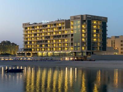 Modernes Hotel mit vielen beleuchteten Fenstern am ruhigen Strand bei Dämmerung.