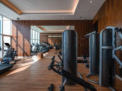 Moderner Fitnessraum mit Holzboden, großen Fenstern und mehreren Trainingsgeräten.