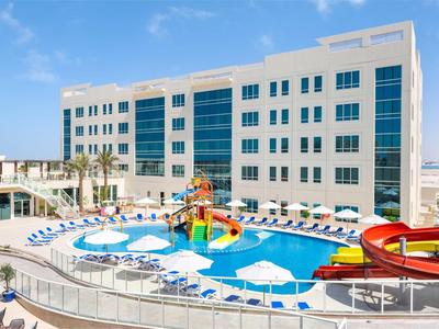 Moderner Hotelkomplex mit Außenpool, Wasserrutschen und Sonnenschirmen unter blauem Himmel