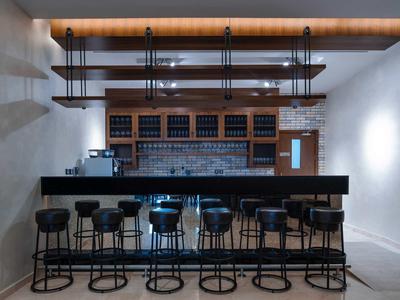 Moderner Barbereich mit schwarzem Tresen, fünf hohen Stühlen und Holzregalen an weißer Wand.