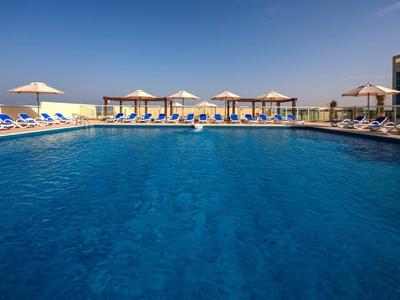 Großes blaues Schwimmbecken mit Liegestühlen und Sonnenschirmen unter klarem Himmel.