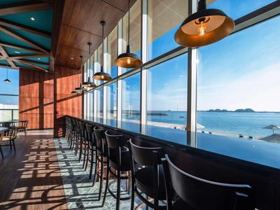 Moderne Bar mit schwarzen Hockern und großen Fenstern, Blick auf das blaue Meer und Inseln.