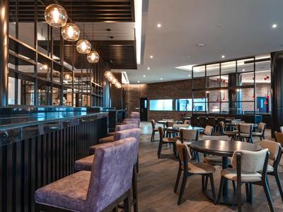 Moderner Gastraum mit runden Tischen, Polsterstühlen und glühenden Hängeleuchten an der Decke.